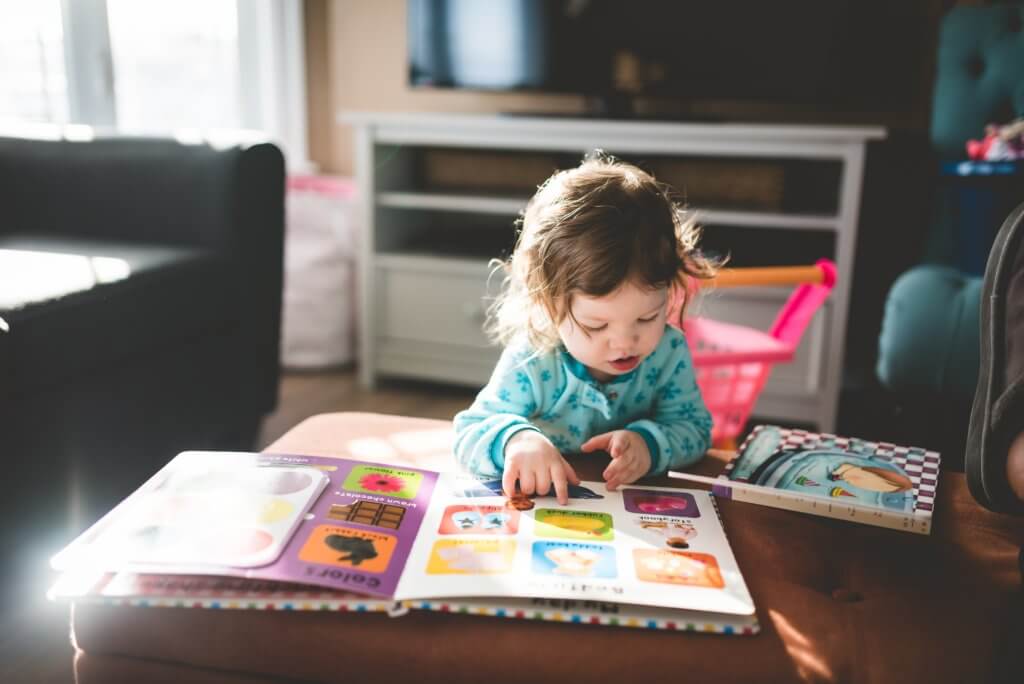 Toddler sitting at a table looking at a children's book.